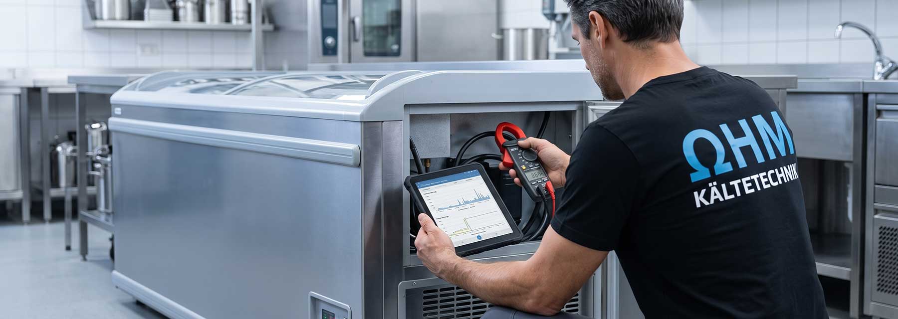 Techniker von Ohm Kältetechnik misst mit Strommesszange und Tablet den Stromverbrauch und die Laufzeiten an einem geöffneten Gastro-Kühlgerät